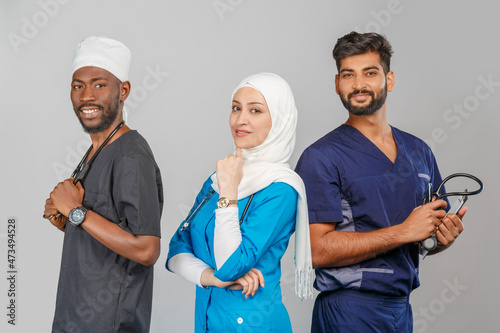 Portrait of positive healthcare workers standing in the hallway and looking at the camera. Group of medics smiling over gray background. muslim doctor woman on background of african and indian doctor photo