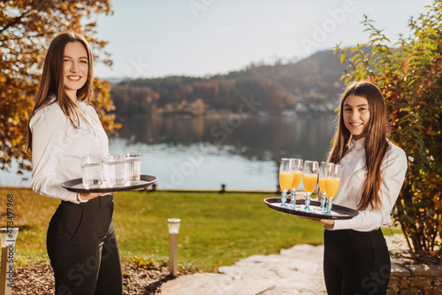 Waitresses standing with tray in garden by lake during sunny day