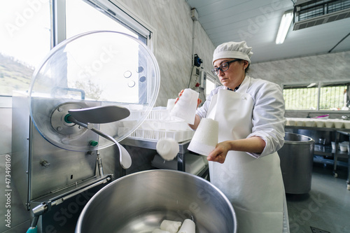 Mature chef putting cheese in machinery from container at dairy factory photo