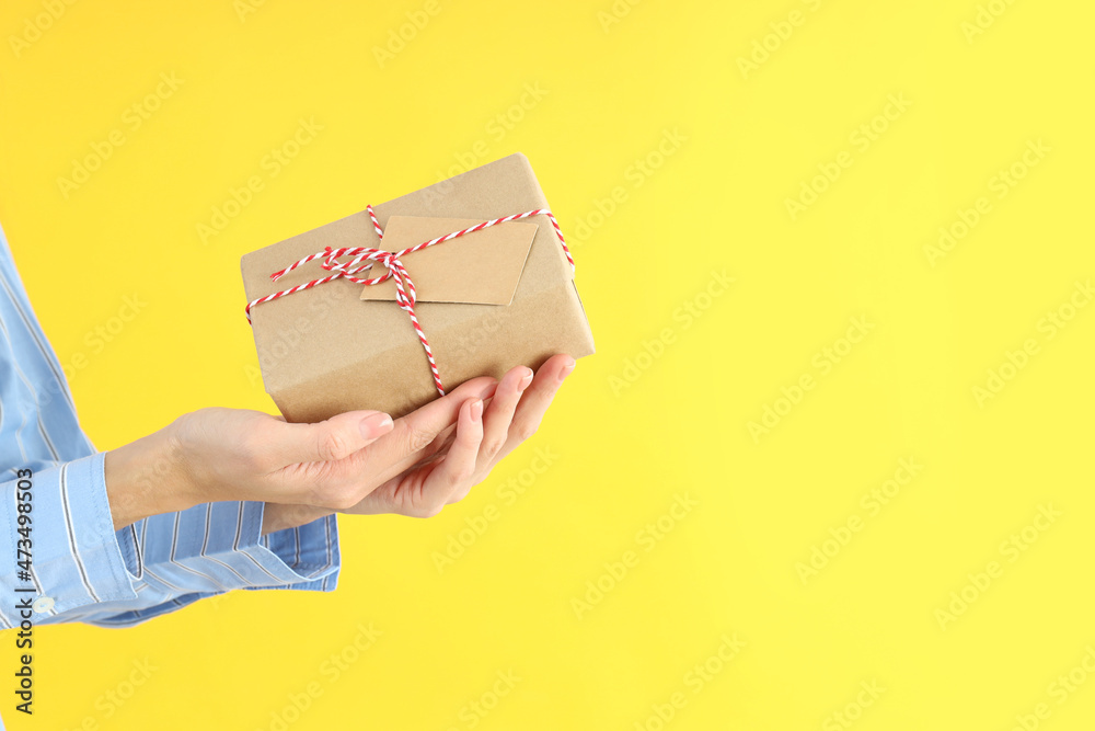 Female hands holding gift box on yellow background, space for text Female hands holding gift box on yellow background, space for text