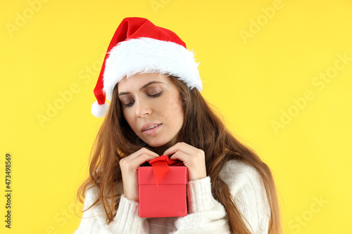 Attractive woman in Santa hat holds gift box on yellow background