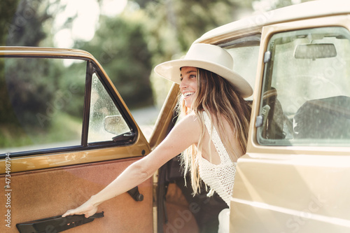 Smiling woman with hat closing door of car photo