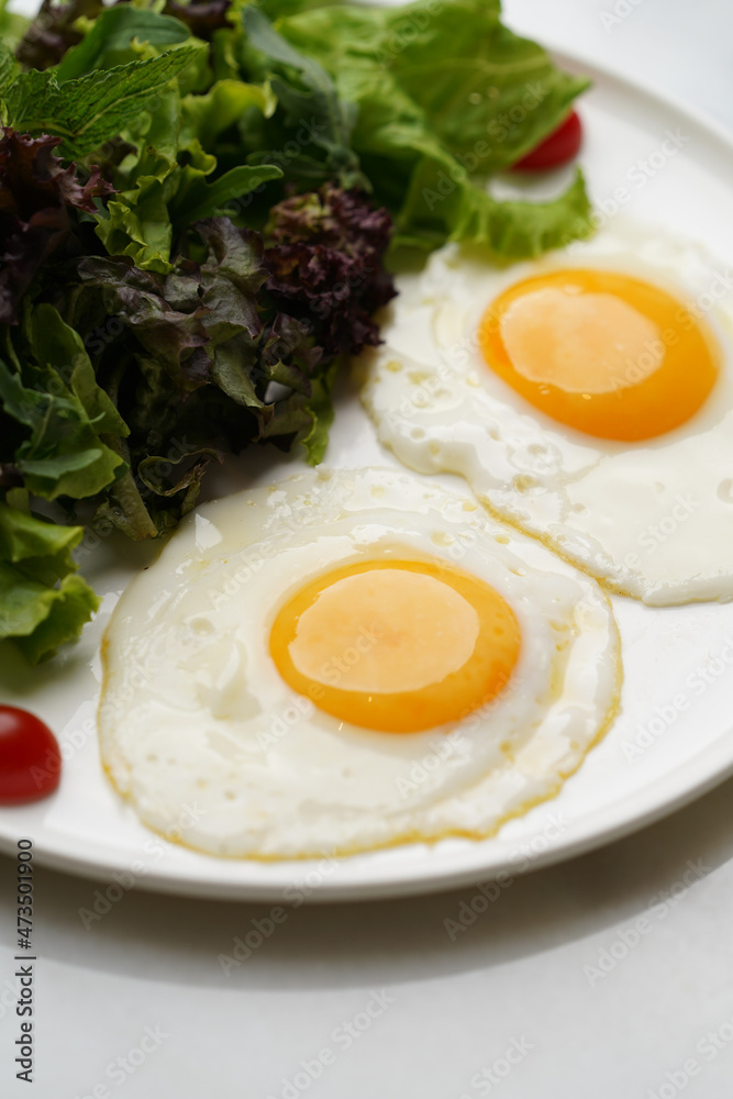 Two fried eggs and fresh salad leaves in white plate Two fried eggs and fresh salad leaves in white plate