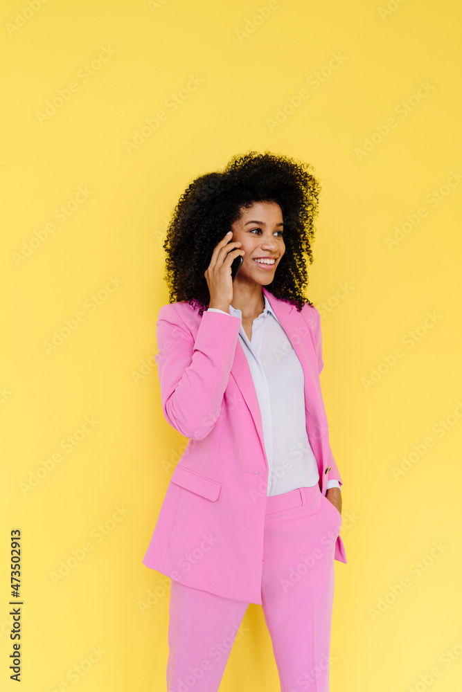 Smiling businesswoman looking away while talking on smart phone in front of yellow background Smiling businesswoman looking away while talking on smart phone in front of yellow background