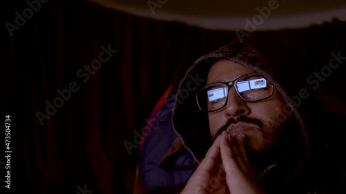 A close up shot of an Indian man conducting undercover surveillance as he watches multiple computer screens looking for information in a dark room photo