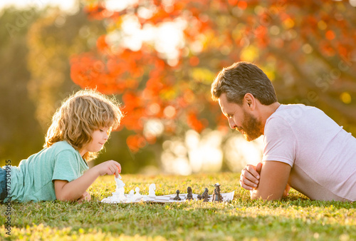 happy family of father man and son kid playing chess on green grass in park outdoor, fatherhood