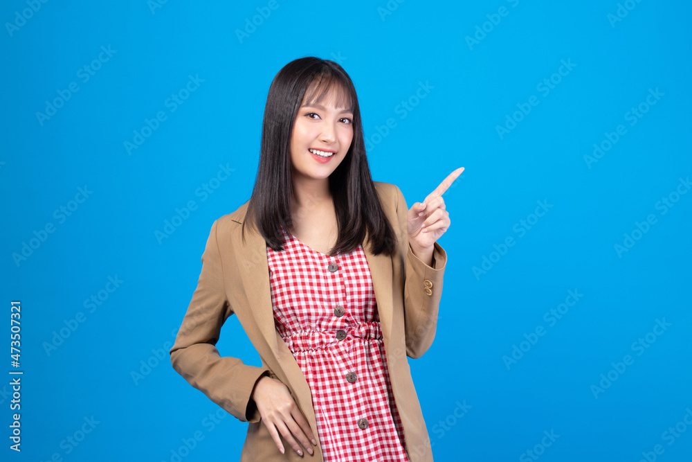 Beautiful Asian woman wearing casual clothes smile and pointing finger at copy space isolated on blue background studio portrait. Beautiful Asian woman wearing casual clothes smile and pointing finger at copy space isolated on blue background studio portrait.