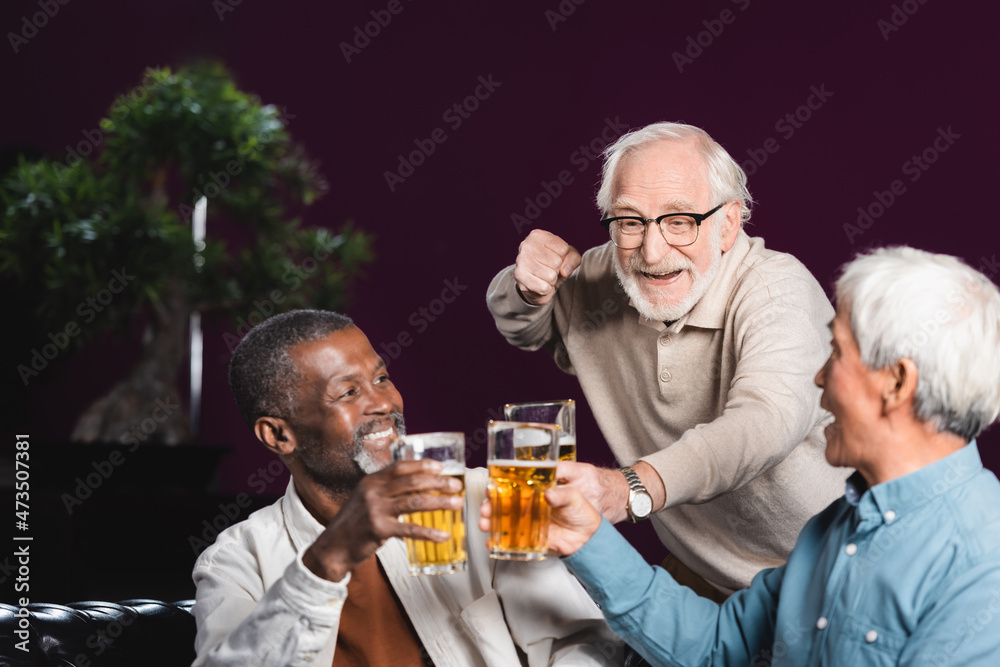 excited senior man showing win gesture while clinking glasses of beer with friends in pub excited senior man showing win gesture while clinking glasses of beer with friends in pub