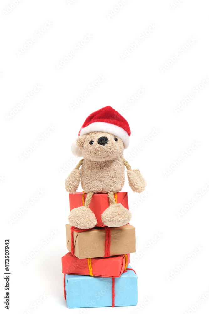 Small teddy bear in a Santa Claus hat sits on boxes with Christmas gifts.On a white background.