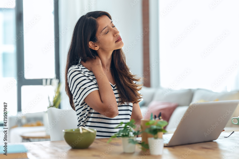 Tired business woman with neck pain looking uncomfortable while working with laptop in living room at home. Tired business woman with neck pain looking uncomfortable while working with laptop in living room at home.