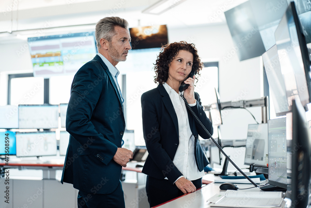Businesswoman talking on telephone while standing with colleague in control room
