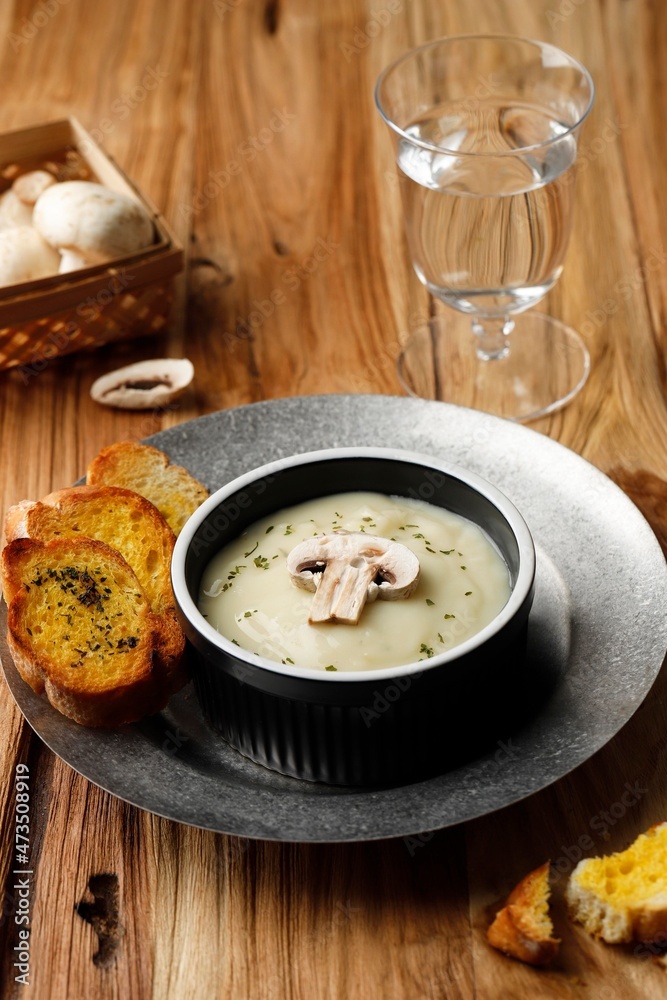 Mushroom Creamy Soup with Crispy Garlic Bread Baguette, Serve on Black Ceramic Bowl or Ramequin, on Rustic Brown Wooden Table.