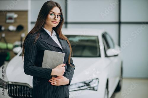 Young sales woman at carshowroom standing by the car photo