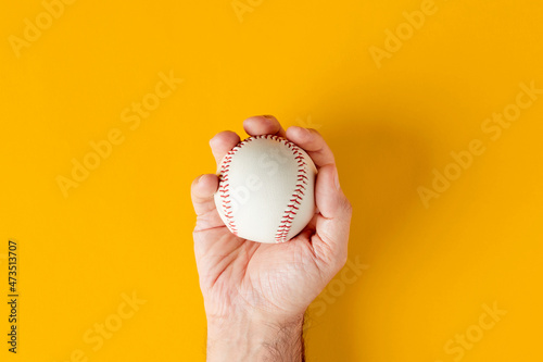 Photography Male hand holds a baseball ball on yellow background.