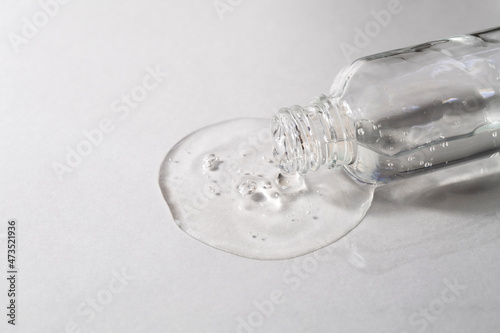 Transparent facial serum with hyaluronic acid pouring from glass bottle on grey background. Cosmetic product with collagen closeup. Beauty concept.