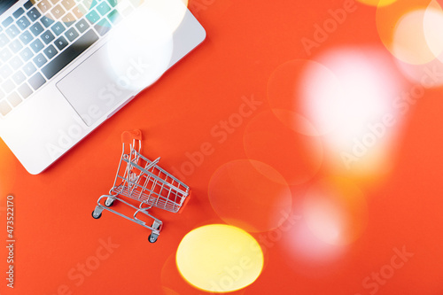 Christmas online shopping on laptop with credit card. New year decorations candy canes, shopping cart and presents box top view flat lay on red background. Merry Xmas winter holidays sales concept.