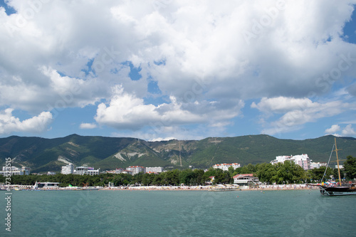 Beautiful white clouds on a blue sky and mountains in the sea with a city, a yacht is visible.