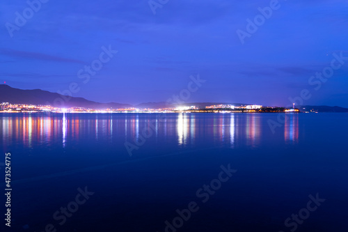 Evening city with lights on the background of mountains and sea, stone coast and blue sky.