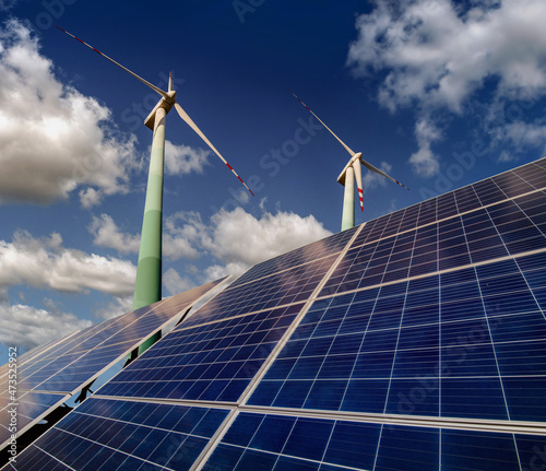 Solar panels and wind turbines closeup with clouds background, bottom up view