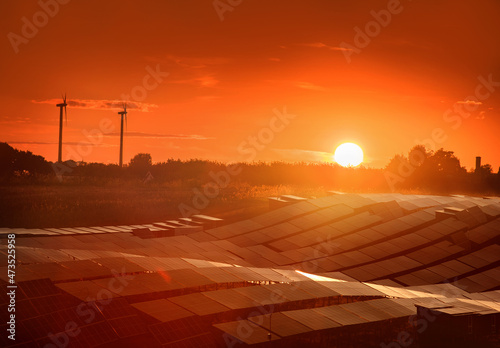 Solar panel station and silhouettes of wind turbines against the evening sky ...
