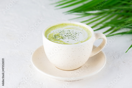 Matcha latte tea with coconut milk and hemp seeds in a mug on the background of a palm branch.