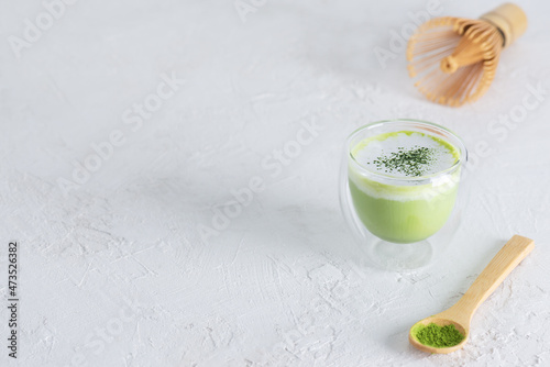 Matcha latte tea with coconut milk and hemp seeds in a glass with powder and a whisk on a light background. Horizontal orientation, top view.
