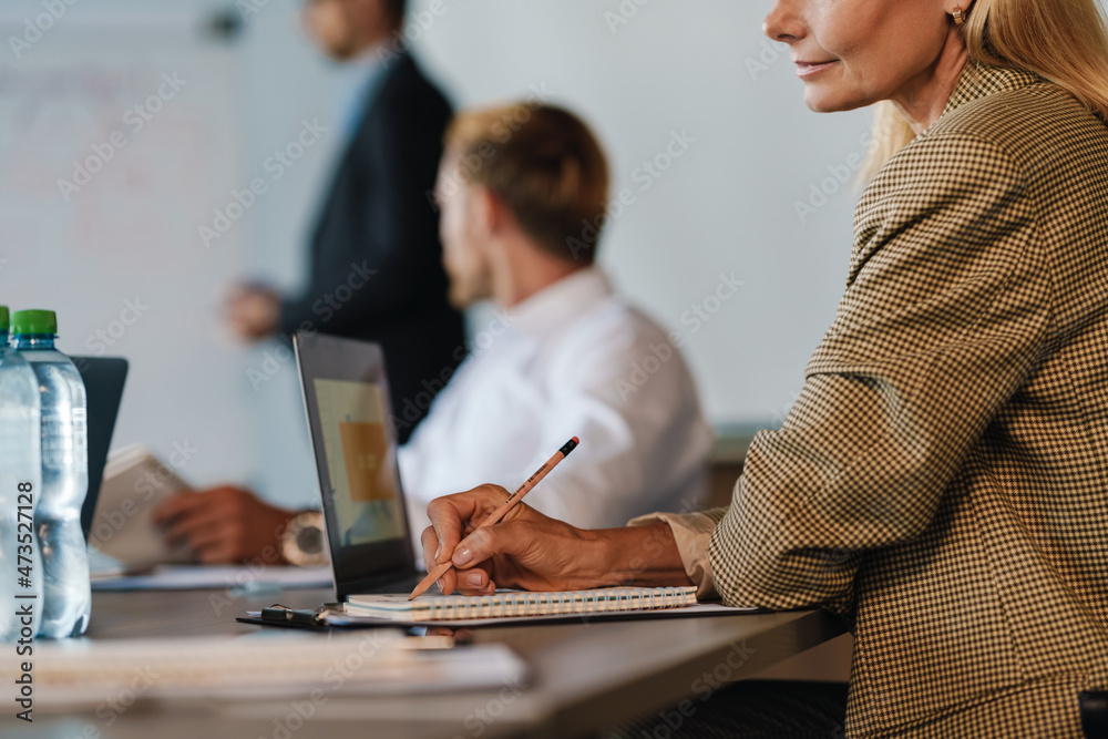 White woman writing down notes and using laptop during meeting White woman writing down notes and using laptop during meeting