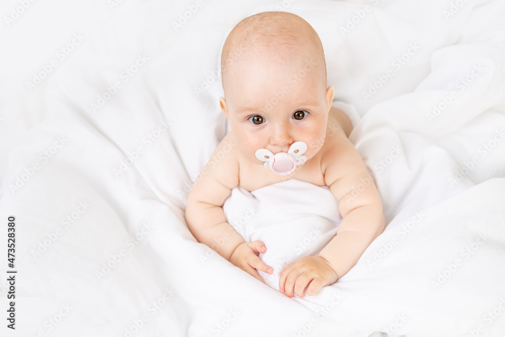 baby girl with a pacifier in a crib on a white cotton bed six months old baby girl with a pacifier in a crib on a white cotton bed six months old