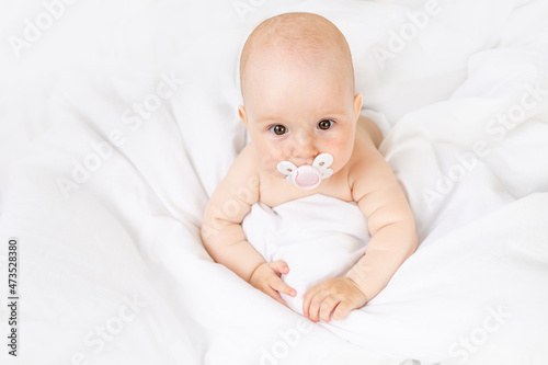 baby girl with a pacifier in a crib on a white cotton bed six months old