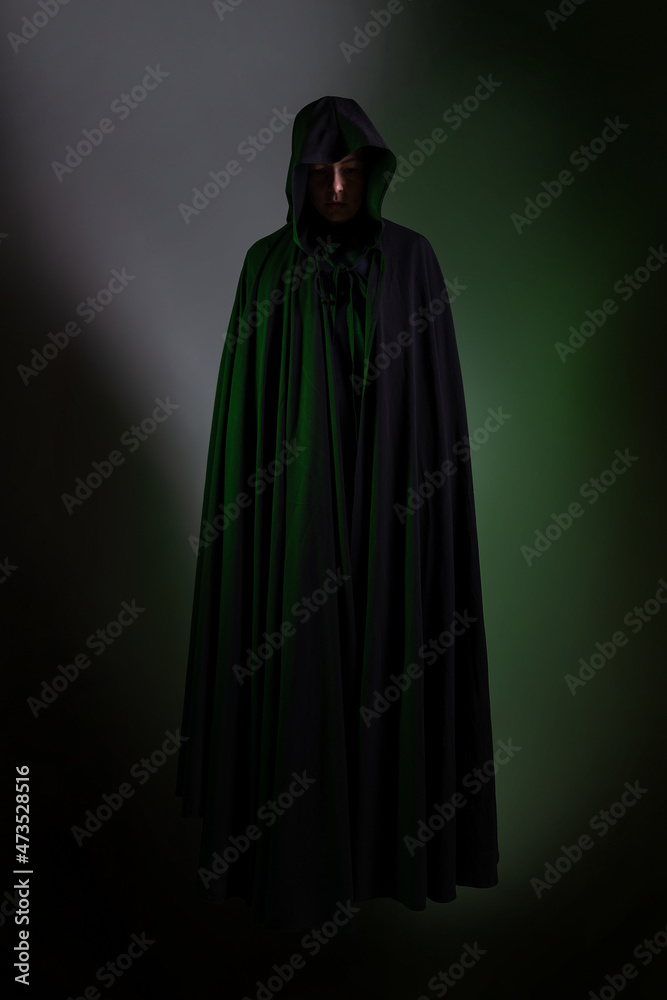 A flying mystical vampire in a black hoodie, a figure hovering in the air, a face hidden by a hood, a dark background green backlight