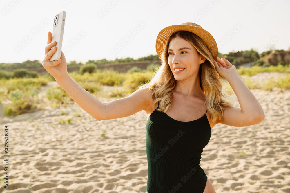 Young blonde woman wearing swimsuit taking selfie on cellphone