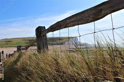 Wooden fence with wire atop seagrass with the seven sisters chalk cliffs in the distance (England) photo