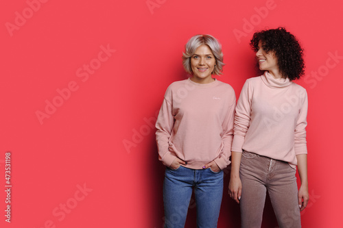 Portrait of two smiling caucasian women standing against pink background with copyspace. photo