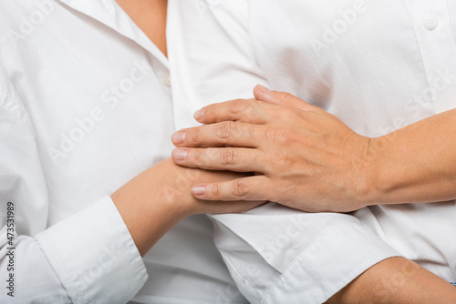 cropped view of young daughter and mother in white shirts holding hands