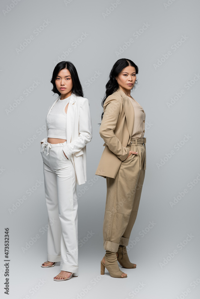 full length of stylish asian mother and young adult daughter in suits posing on grey full length of stylish asian mother and young adult daughter in suits posing on grey