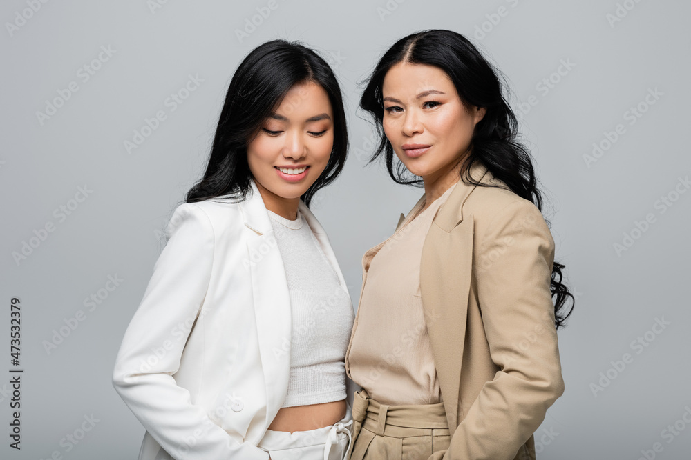 stylish asian mother and smiling young adult daughter in suit isolated on grey stylish asian mother and smiling young adult daughter in suit isolated on grey