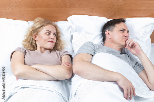 Two in bed, a woman looks with suspicion at a man who has turned away in the other direction. Relationship concept photo
