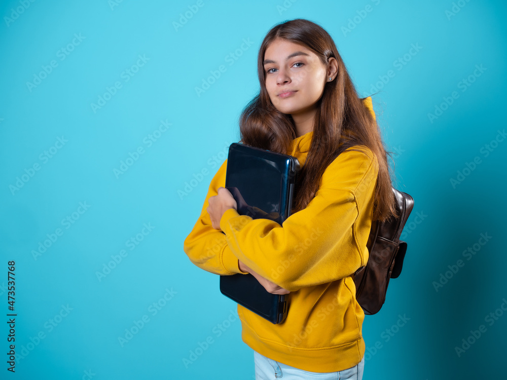 Internet work and e-education, a student or a freelancer works remotely. A student with a laptop in her hands, a young brunette in a yellow hoodie on a blue background Internet work and e-education, a student or a freelancer works remotely. A student with a laptop in her hands, a young brunette in a yellow hoodie on a blue background