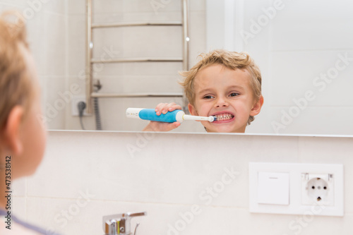 A five-year-old boy is brushing his teeth in the bathroom. A five-year-old boy, a European on the street, brushes his teeth in the bathroom in front of the mirror.