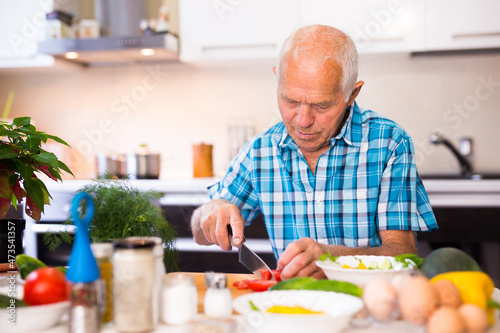 senor man preparing fresh vegetable salad at home in the kitchen