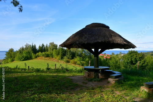 Close up on a small resting spot with its rood made out of sticks and thatch located on the top of a tall hil with many meadows, forests and fields seen in the distance on a sunny summer day in Poland