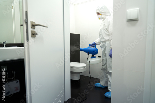 Female sanitation worker spraying disinfective chemical in public toilet at hospital during COVID-19 photo