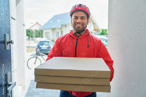 Male delivery person holding pizza box while standing at doorway photo