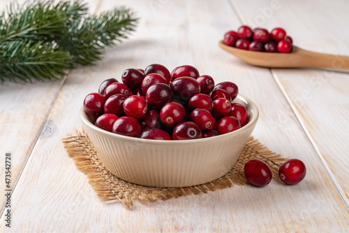 Ripe red cranberries in a beige bowl over white rustic wooden table. Ingredient for cooking Thanksgiving and Christmas dishes and desserts. Fresh wild berries for healthy eating.