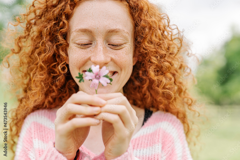 Smiling redhead woman with curly hair holding flower
