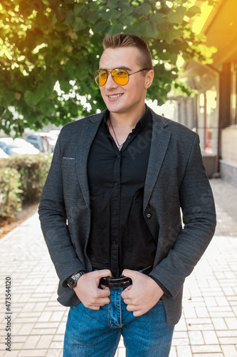 Stylish positive smiling young attractive guy of European appearance businessman portrait in jacket, shirt and jeans, in sunglasses on the street outdoor