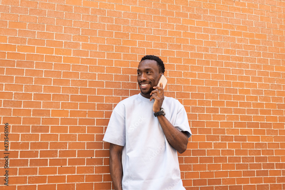 Man looking away while talking on smart phone in front of brick wall Man looking away while talking on smart phone in front of brick wall