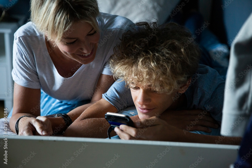 Son sharing smart phone with smiling mother while on bed at home Son sharing smart phone with smiling mother while on bed at home