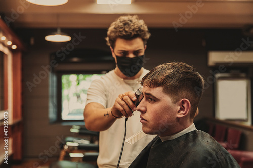 Young man getting haircut by male barber in salon during COVID-19 outbreak photo