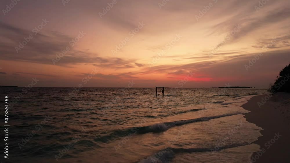 Drone shot fly over evening sea, orange sunset and person on a swing. Aerial shot of beautiful, panoramic view of ocean water and beach in Maldives. Concept of trip Drone shot fly over evening sea, orange sunset and person on a swing. Aerial shot of beautiful, panoramic view of ocean water and beach in Maldives. Concept of trip